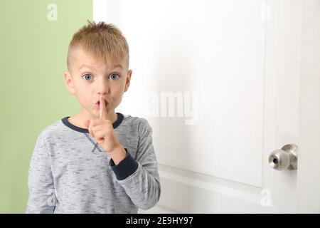Bel ragazzo che mostra un gesto di silenzio vicino alla porta chiusa Foto Stock