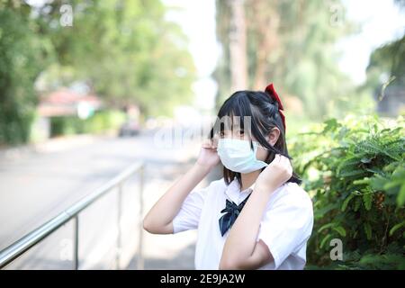 Ragazza asiatica della scuola con maschera in città passerella Foto Stock