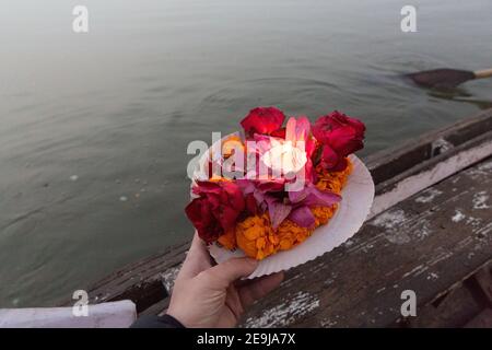 Mano che mette l'offerta di candela e fiori sul fiume Gange Foto Stock