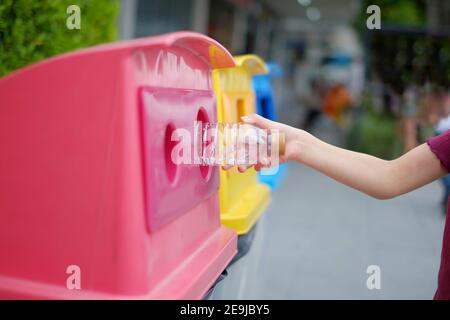 Un primo piano immagine di una ragazza asiatica carina gettando via una bottiglia vuota di plastica acqua su un cestino di riciclaggio che ha ordinato i rifiuti in 3 gruppi, ricicla Foto Stock