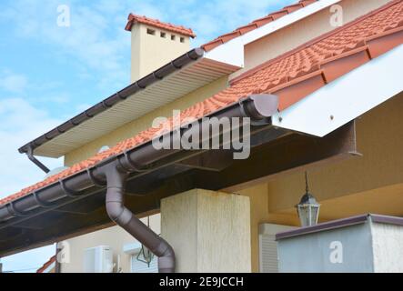 Primo piano sul sistema di tubazioni per gocciolatoio con supporti e tubo di scarico gocciolatoio. Casa residenziale tetto Gutter. Foto Stock
