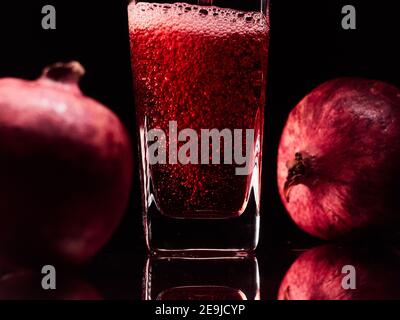 Vetro nell'illuminazione a basso livello con due melograni e succo. Foto di alta qualità Foto Stock