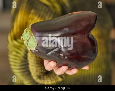 La brutta melanzana a forma di cuore tiene in mano. Divertente, alterato vegetale o concetto di spreco di cibo Foto Stock