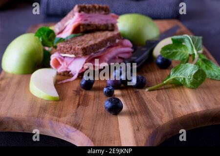 Panino integrale con prosciutto servito con fette di mele fresche e. mirtilli su una tavola di legno Foto Stock