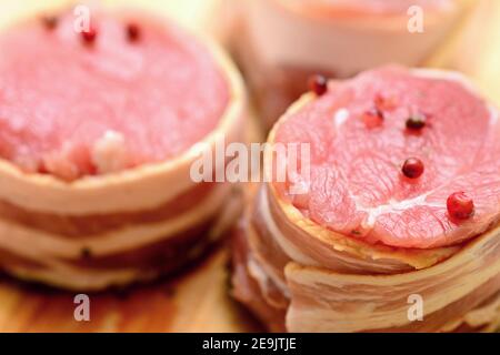 Closeup di medaglioni di filetto di maiale freschi e crudi con pancetta cosparsi di pepe rosso intero. Foto Stock