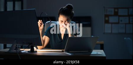 Donna con occhi stanchi asciutti che lavorano tardi di notte utilizzando Computer in ufficio Foto Stock