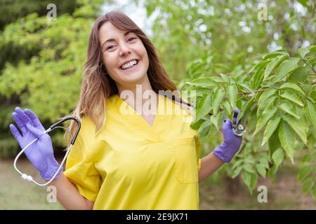 Ritratto di giovane e sorridente dottore tenendo felice con le mani uno stetoscopio. È all'aperto in natura. Spazio per il testo. Foto Stock