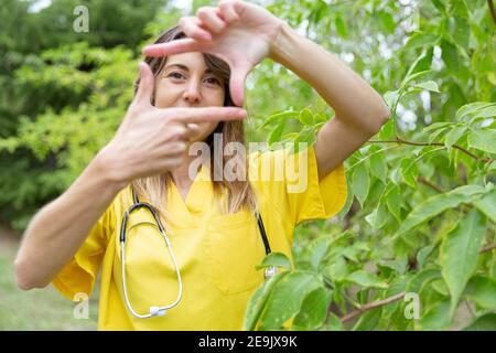 Giovane infermiera femminile che incornicia il viso con le mani come un autoritratto. È in natura. Spazio per il testo. Foto Stock