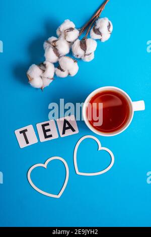 Fuoco selettivo: Tè nero di Ceylon in una tazza bianca su un fondo di carta comune blu. copyspace. Lettere di cartone disposte nella parola tè in inglese Foto Stock