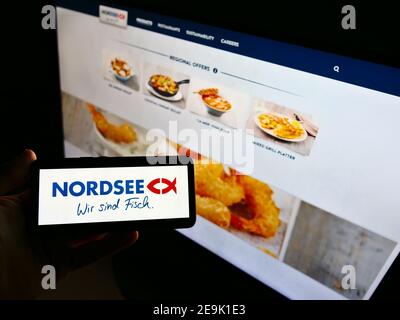 Persona che tiene il cellulare con il logo della catena tedesca di fast-food Nordsee GmbH (frutti di mare) in esposizione davanti al sito web. Mettere a fuoco lo schermo del telefono. Foto Stock