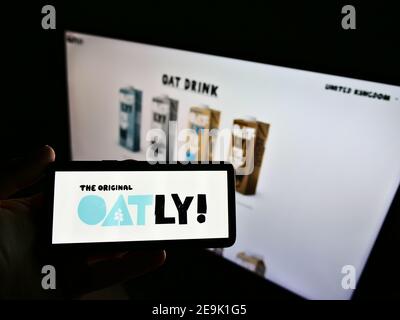 Persona che detiene smartphone con il logo della società svedese di alimenti vegani (prodotti di avena) Oatly AB in esposizione davanti al sito web. Mettere a fuoco lo schermo del telefono. Foto Stock