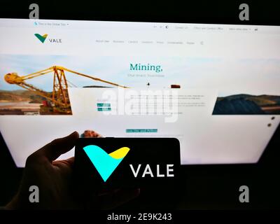 Persona che detiene smartphone con logo della società mineraria e logistica brasiliana vale S.A. in esposizione davanti al sito web. Mettere a fuoco lo schermo del telefono. Foto Stock