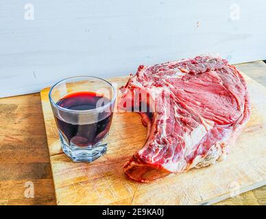 Bistecca di manzo alle ossa, ben stagionata, pronta per il vostro barbecue e pranzo, bistecca fiorentina, con un bicchiere di buon vino rosso genuino Foto Stock