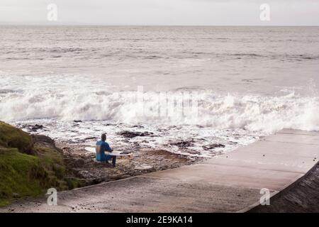 Silhouette di surfista seduto con una tavola da surf sulla spiaggia. Foto Stock