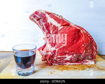 Bistecca di manzo alle ossa, ben stagionata, pronta per il vostro barbecue e pranzo, bistecca fiorentina, con un bicchiere di buon vino rosso genuino Foto Stock