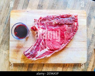 Bistecca di manzo alle ossa, ben stagionata, pronta per il vostro barbecue e pranzo, bistecca fiorentina, con un bicchiere di buon vino rosso genuino Foto Stock