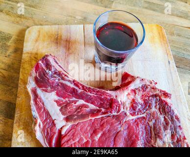 Bistecca di manzo alle ossa, ben stagionata, pronta per il vostro barbecue e pranzo, bistecca fiorentina, con un bicchiere di buon vino rosso genuino Foto Stock