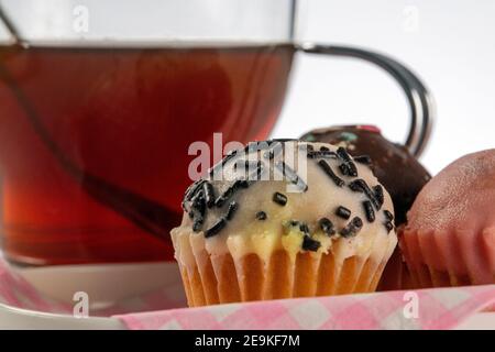 Deliziosi cupcake assortiti su un vassoio con un tovagliolo rosa a scacchi, accompagnati da un bicchiere di tè Foto Stock