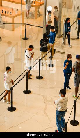 Vista dall'alto di una coda di clienti in piedi in una fila socialmente distanziata fuori da un negozio di mele in un centro commerciale. Tutti indossano una maschera. Foto Stock