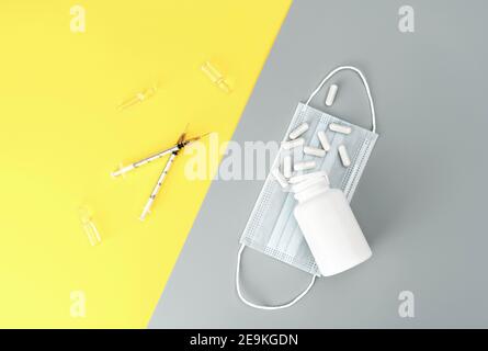 Flacone mock-up con pillole, siringhe, fiale e maschera medica su sfondo giallo e grigio alla moda. Medicina di base. Vaccino del coronavirus Foto Stock