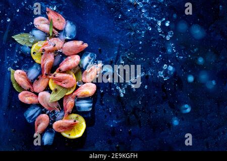 Gamberi crudi con ghiaccio e limone su sfondo blu, vista dall'alto. Pesce. Con spazio copia Foto Stock