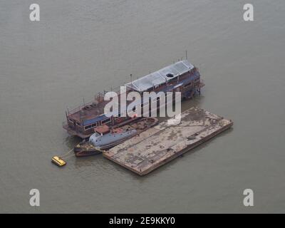 vista aerea di un edificio galleggiante e molo con un piccola imbarcazione industriale su un fiume grigio fangoso Foto Stock