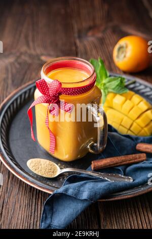 Mango speziato e frullato di persimon con zenzero e cannella in un vaso di vetro per l'immunità e la digestione su legno rustico sfondo Foto Stock