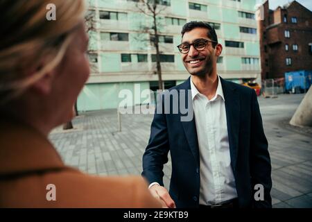 Razza mista uomo d'affari maschile scuotendo le mani con la donna bionda collega Foto Stock