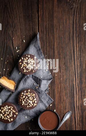 Trattamento croccante freddo, tazze di cioccolato con ripieno di caramello e burro di arachidi, cosparse di noci tritate su rustico fondo di legno Foto Stock