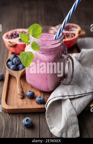 Frullato di melograno e mirtillo mescolato con yogurt e latte di mandorle, servito in un vaso di vetro su rustico sfondo di legno Foto Stock