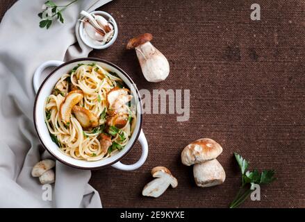 Pasta con funghi porcini freschi e prezzemolo in bianco vaso d'epoca su una tovaglia marrone Foto Stock