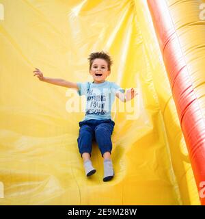 Ragazzo sorridente che gioca su uno scivolo gonfiabile Foto Stock