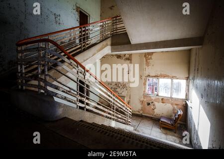 Abbandonata costruzione creepy scala di moody scuro in fatiscente corsa giù vecchia rovina deserta della scuola ospedaliera con una sola sedia vuota all'interno sulle scale Foto Stock