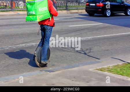 Un giovane di un servizio di consegna del cibo con uno zaino verde sulla schiena corre un monociclo e consegna il cibo. Foto Stock