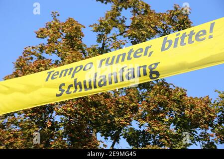 Bandiera sopra la strada con le lettere tedesche „Slow down please, scuola starter" (Germania) Foto Stock