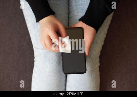Donna pulisce lo schermo di un telefono cellulare con un tovagliolo di alcol a casa, vista dall'alto. Foto Stock