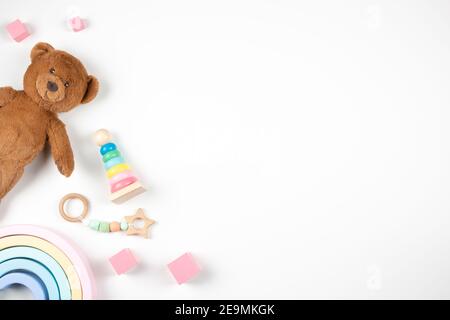 I giocattoli per bambini sono incorniciati su sfondo bianco. Teddy bard e giocattoli educativi in legno sulla scrivania. Vista dall'alto. Disposizione piatta Foto Stock