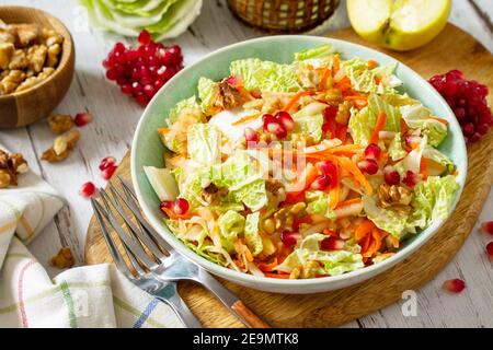 Insalata dietetica verdure fresche di cavolo cinese, carote, mela, noci e melograno con condimento vinaigrette su un tavolo di legno bianco. Foto Stock