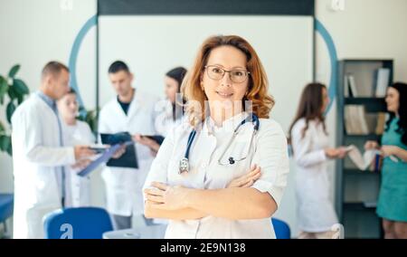 Ritratto di sorridente medico femminile soddisfatto del suo lavoro in un ospedale sanitario. Professionisti medici al lavoro. Dottore pediatra femminile in bianco Foto Stock