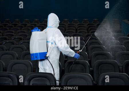 Operaio in indumenti protettivi contro il coronavirus con attrezzatura speciale per la disinfezione sala di pulizia cinema. Concetto di protezione contro i virus. Foto Stock