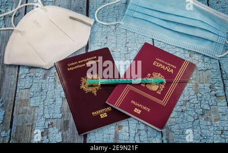 Concetto di turismo vaccinale Covid-19. Vista dall'alto di due passaporti, spagnolo e francese, con siringa e maschere protettive su un tavolo blu. Foto Stock