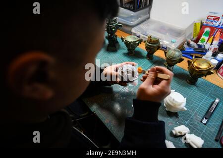 (210205) -- CHENGDU, 5 febbraio 2021 (Xinhua) -- Zeng Zhou pulisce una figura giocattolo alla sua officina a Chengdu, provincia sudoccidentale del Sichuan, 4 febbraio 2021. Zeng Zhou è un designer indipendente di 31 anni che lavora sulla progettazione di personaggi giocattolo. Ispirato da un'esperienza di visita al Museo Sanxingdui di Sichuan, Zeng ha deciso di progettare figure modello che imitano reliquie bronzee delle rovine di Sanxingdui, che si ritiene siano resti del regno di Shu risalenti da 2,600 anni a 4,800 anni fa, mescolando la cultura cinese tradizionale con i giocattoli di moda. Zeng Zhou è ora dedicato a ottimizzare il suo design e il suo promotore Foto Stock