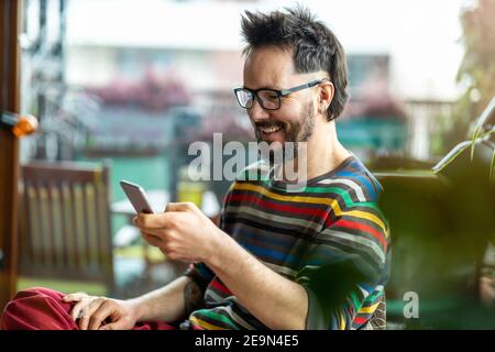 Uomo felice che usa un telefono cellulare a casa Foto Stock
