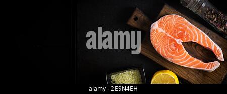 Salmone. Filetto di salmone crudo con ingredienti da cucina, erbe e limone su sfondo nero con spazio copia. Vista dall'alto, overhead, spazio per la copia. Foto Stock