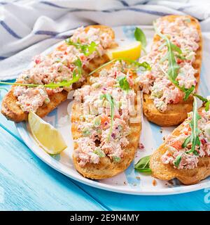 Bruschetta con salmone al forno. Tapas. Sandwich con salsa di salmone, feta, avocado, pomodori e cipolla rossa. Toast con salmone al rione. Foto Stock