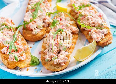 Bruschetta con salmone al forno. Tapas. Sandwich con salsa di salmone, feta, avocado, pomodori e cipolla rossa. Toast con salmone al rione. Foto Stock