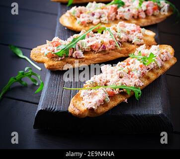 Bruschetta con salmone al forno. Tapas. Sandwich con salsa di salmone, feta, avocado, pomodori e cipolla rossa. Toast con salmone al rione. Foto Stock