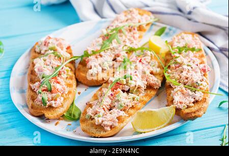 Bruschetta con salmone al forno. Tapas. Sandwich con salsa di salmone, feta, avocado, pomodori e cipolla rossa. Toast con salmone al rione. Foto Stock