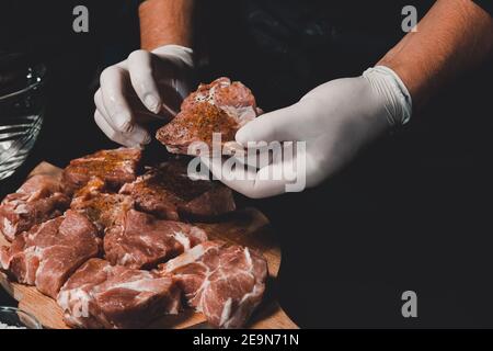 Marinare gli spiedini del collo di maiale, aggiungere sale, curry e basilico alla carne, pezzi di carne su una tavola di legno.2020 Foto Stock