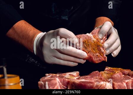 Marinare gli spiedini del collo di maiale, aggiungere sale, curry e basilico alla carne, pezzi di carne su una tavola di legno.2020 Foto Stock